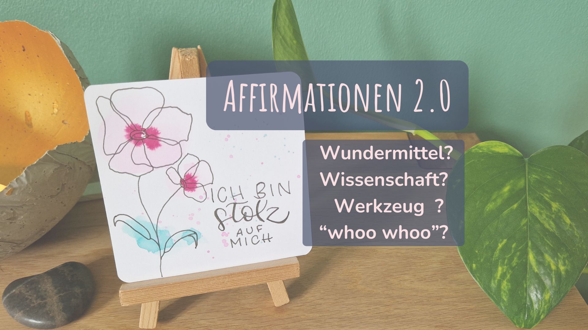 Zu sehen ist eine selbst gestaltete Affirmations-Karte mit dem Text "Ich bin stolz auf mich". Sie steht auf einem Aufsteller, vor einer grünen Wand. Im Hintergrund rechts eine Pflanze, links eine Kerze.