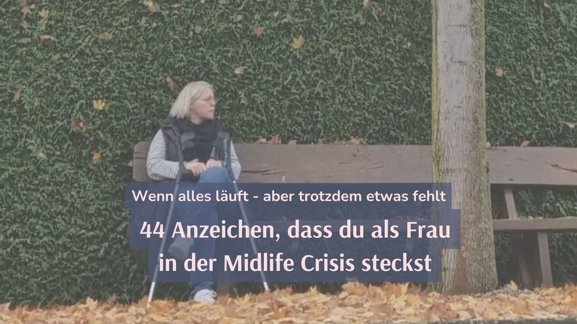 Tina sitzt auf einer Parkbank vor einer grünen Hecke und schaut zur Seite. Zu ihren Füßen liegt gelbes Herbstlaub.