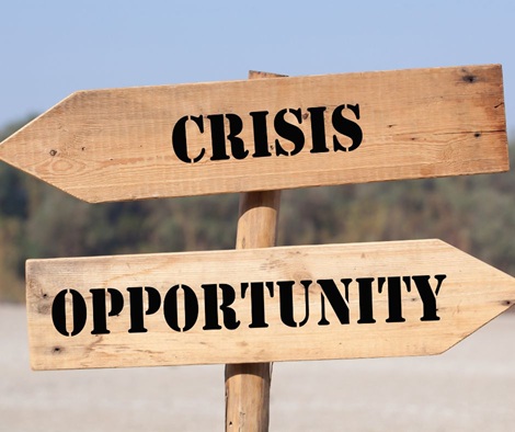 Am Strand steht ein Holzschild mit zwei Pfeilen. Der obere Pfeil zeigt nach links mit dem Text "Crisis" und der untere Pfeil zeigt nach rechts mit dem Text "Opportunity".