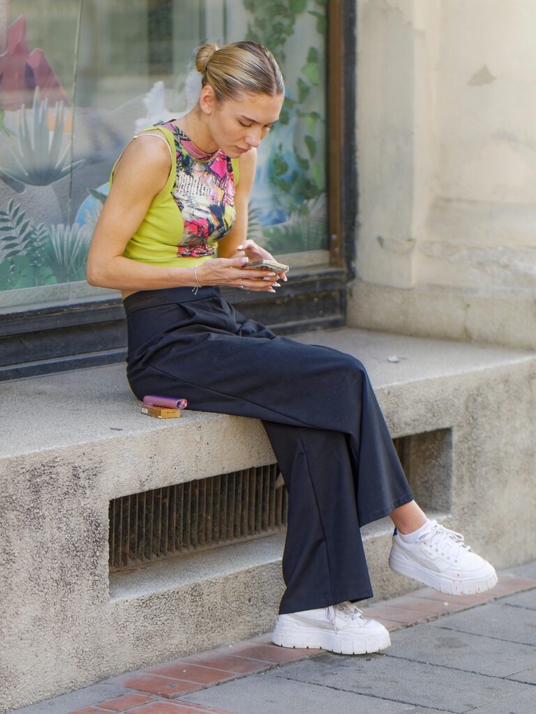 Bild von Mircea Iancu | Surprising Media auf Pixabay.com
EIne Frau sitzt mit ihrem Handy in der Hand auf einer Fensterbank am Gehweg.