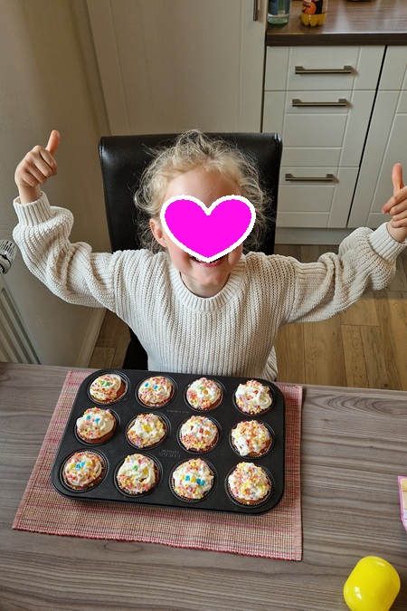Meine Nichte sitzt stolz vor einem Blech mit selbst gebackenen und gestalteten Cupcakes