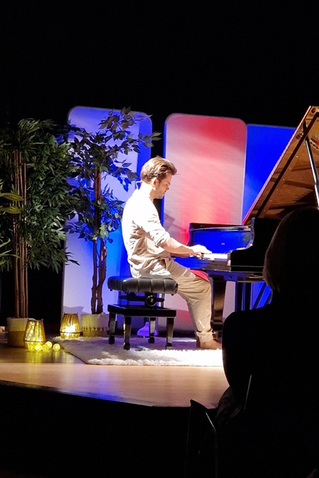 Eine beleuchtete Bühne mit einem Flügel, an dem ein Pianist sitzt